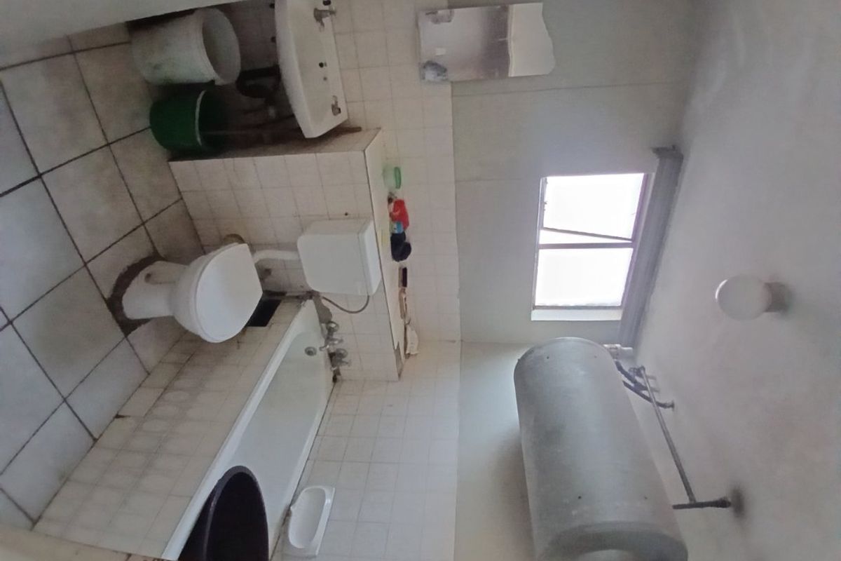 A dated bathroom featuring a bathtub, toilet, and pedestal basin, with visible wear to the wall tiles and overall finishes requiring renovation.