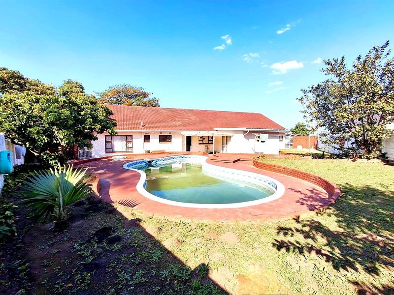 Rear view of the property featuring a swimming pool with a tiled surround, set within a garden area with mature trees.