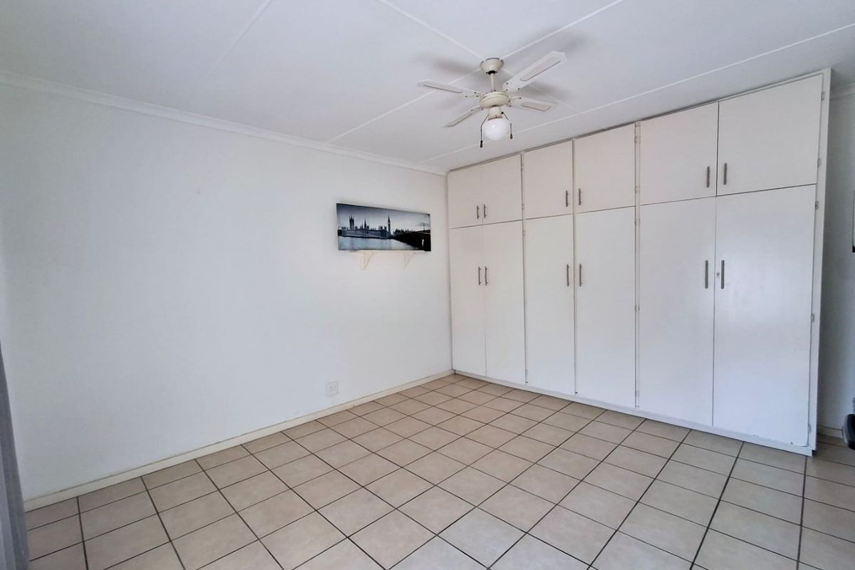 A clean, empty bedroom featuring neutral tiled flooring, a ceiling fan, and extensive built-in cupboard storage.