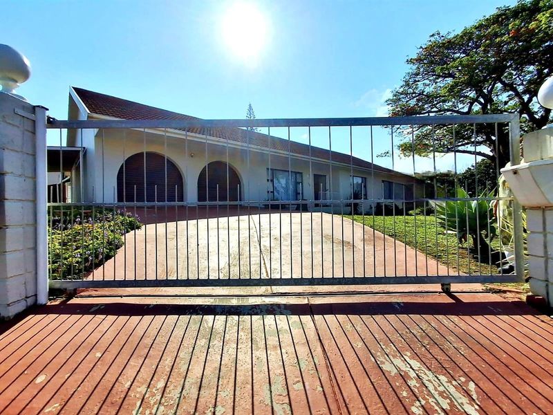 Front view of a single-story house featuring a metal sliding gate, concrete driveway, and distinctive arched windows under a tiled roof.