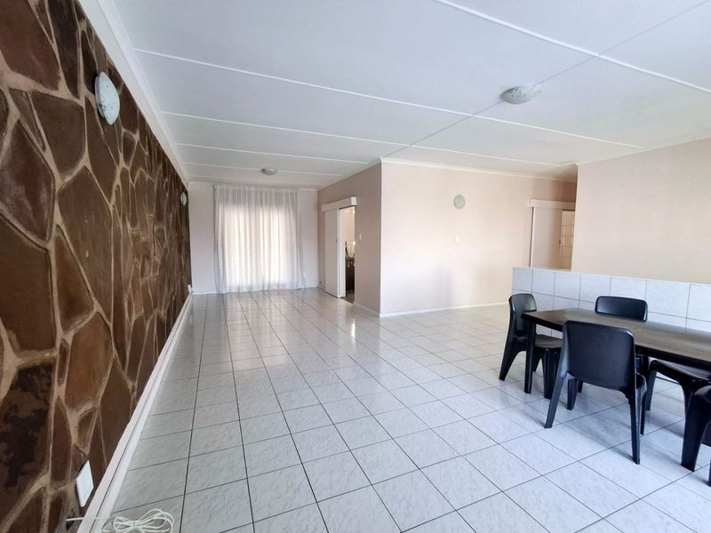 Spacious open-plan living and dining area featuring a prominent stone feature wall, neutral tiled flooring, and direct access to an outdoor space.