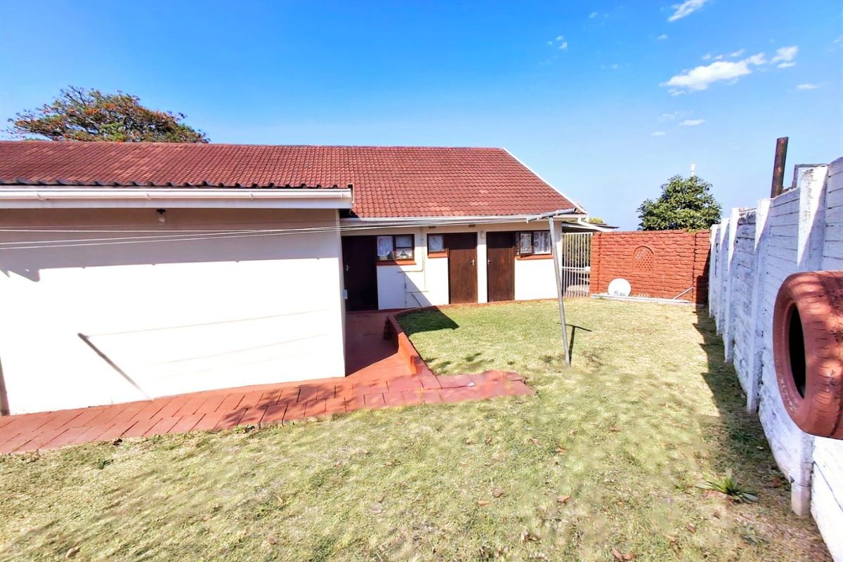 Rear view of the property featuring a tiled roof, paved walkway, and a private garden enclosed by a brick boundary wall.