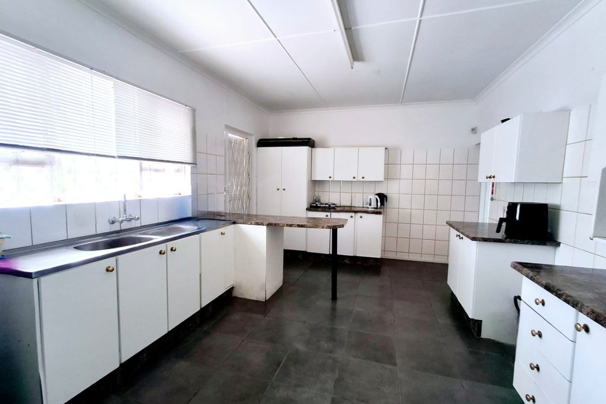 A functional kitchen featuring white cabinetry, dark laminate countertops, tiled splashbacks, and tiled flooring, offering a clean and practical workspace.