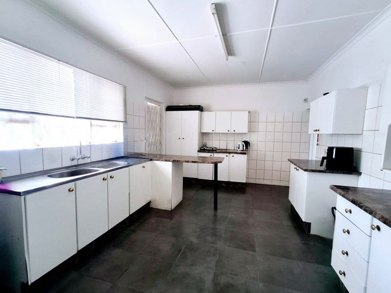 A functional kitchen featuring white cabinetry, dark laminate countertops, tiled splashbacks, and tiled flooring, offering a clean and practical workspace.