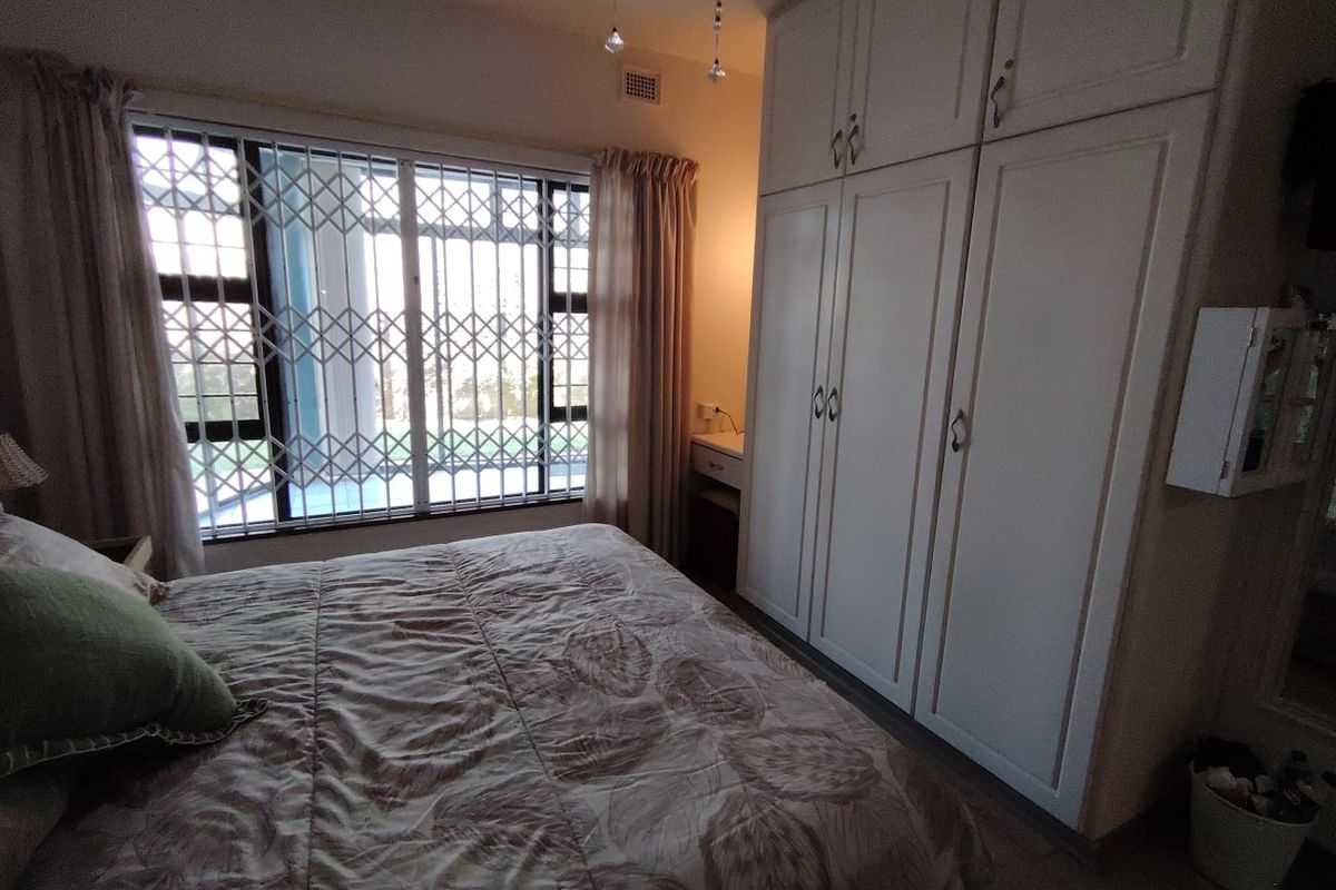 A bedroom featuring built-in cupboards, a built-in vanity, and a window fitted with a security gate.