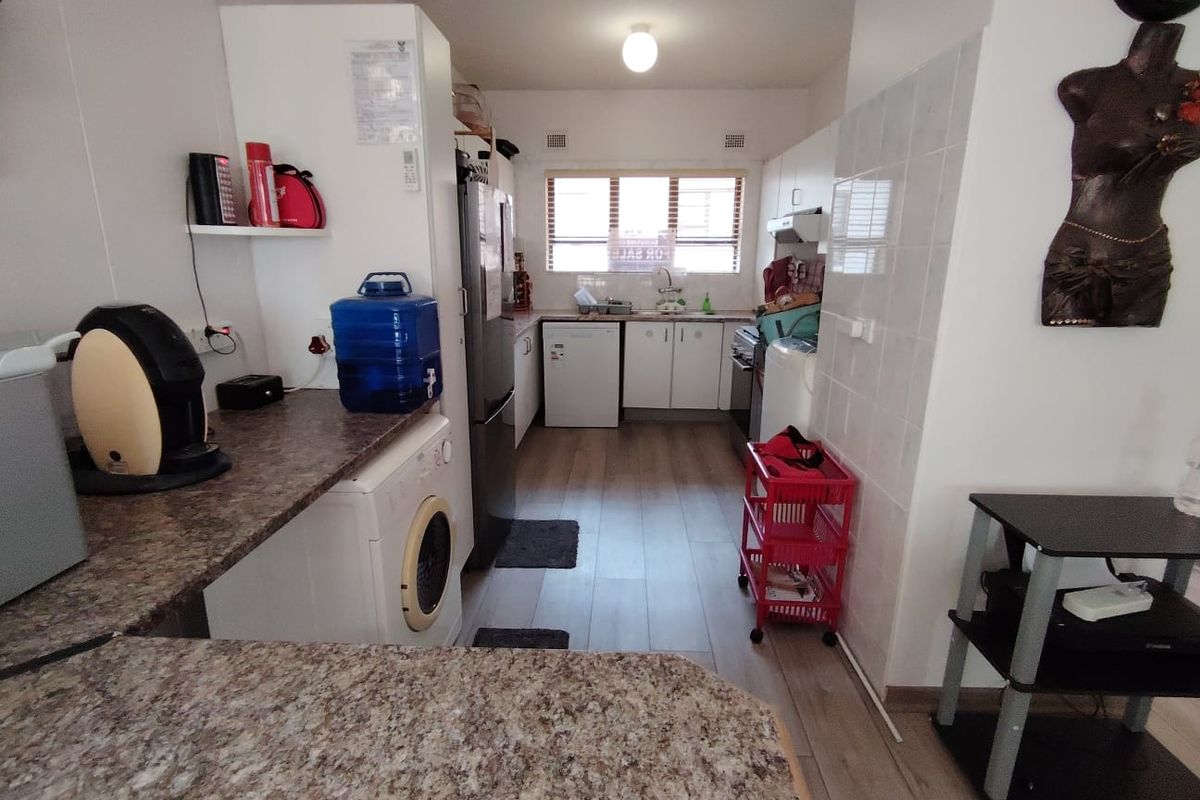 A functional kitchen featuring laminate countertops, built-in cabinetry, tiled splashbacks, and integrated appliance spaces with wood-look laminate flooring.