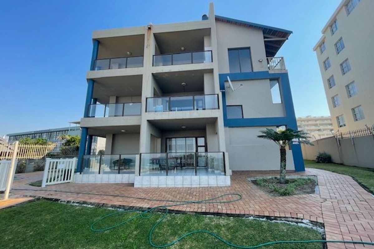 Rear view of a multi-story apartment building featuring private balconies with glass balustrades, sliding doors, and a paved ground-level patio area.