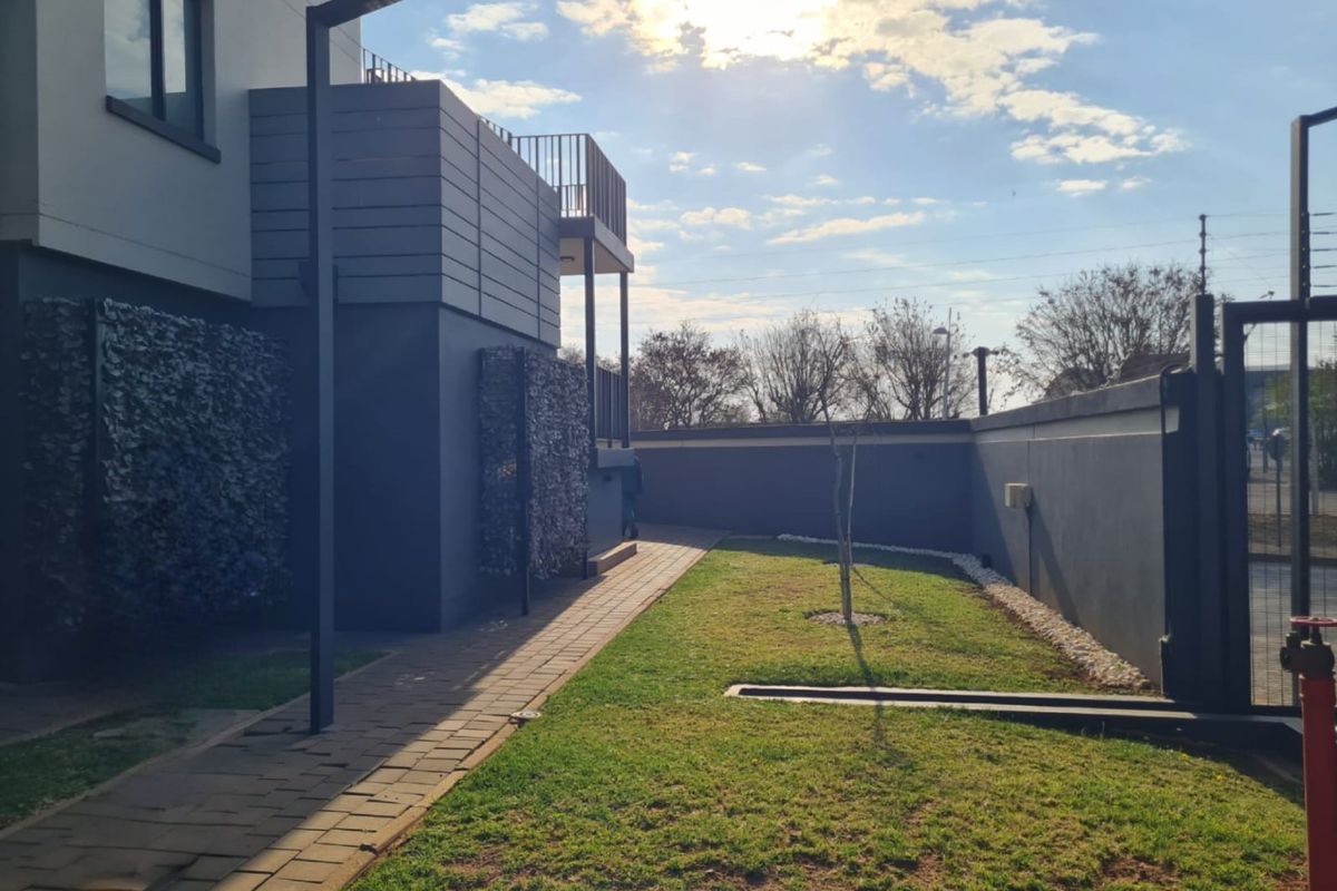 A well-maintained rear exterior area featuring a paved walkway, landscaped garden, and boundary wall, providing a private outdoor space for the apartment.