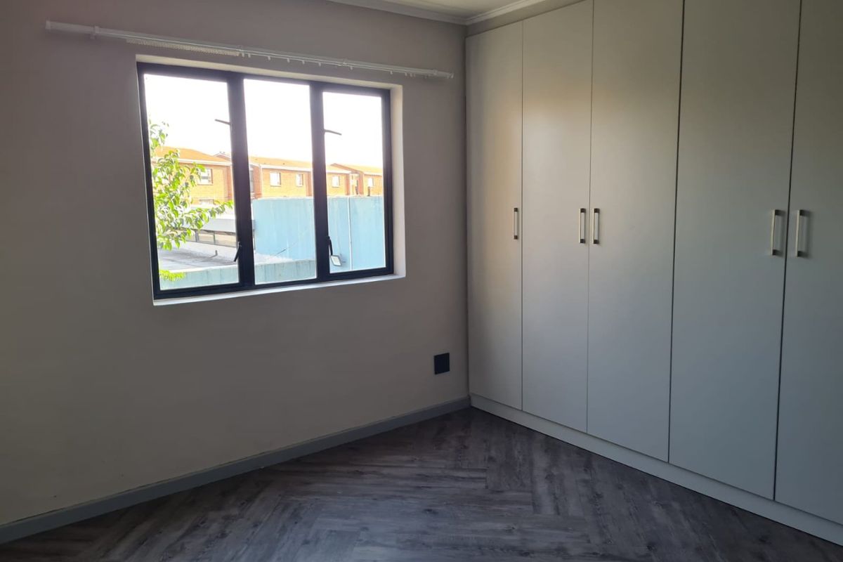 A bright, empty bedroom featuring modern herringbone vinyl flooring and extensive built-in cupboard storage with a neutral finish.