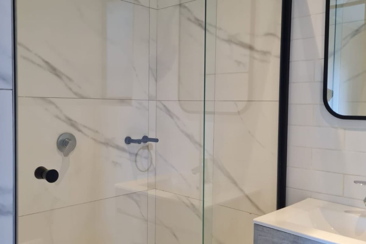 Modern bathroom featuring a walk-in shower with marble-look tiling, black frame accents, and a contemporary vanity unit.