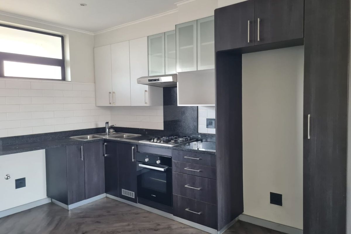 Modern kitchen featuring dark wood cabinetry, granite countertops, built-in gas hob, oven, extractor fan, and subway tile backsplash with laminate flooring.