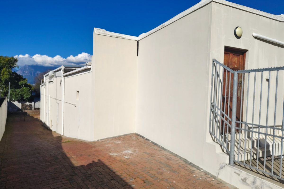 Rear exterior view of the commercial property featuring brick paving, a secure metal gate, and a timber entrance door.