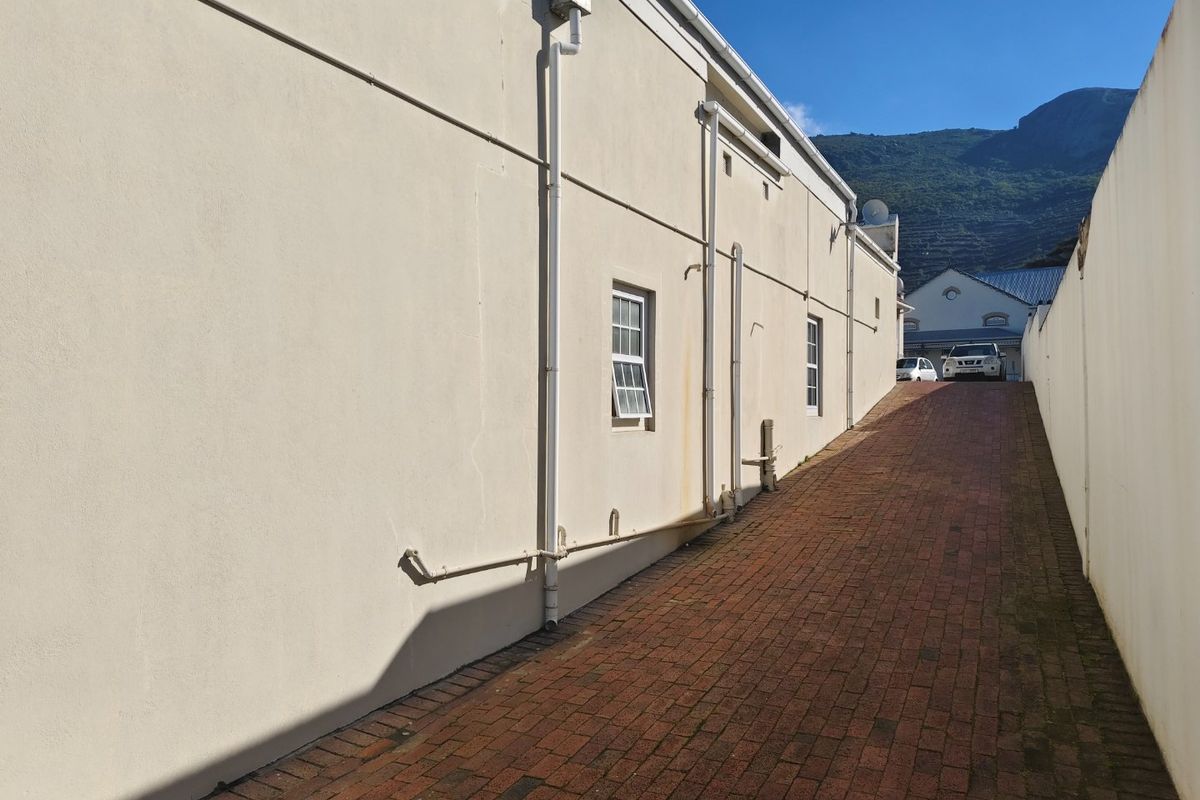 A side view of the commercial property featuring a brick-paved driveway, exterior wall with plumbing fixtures, and sash windows.