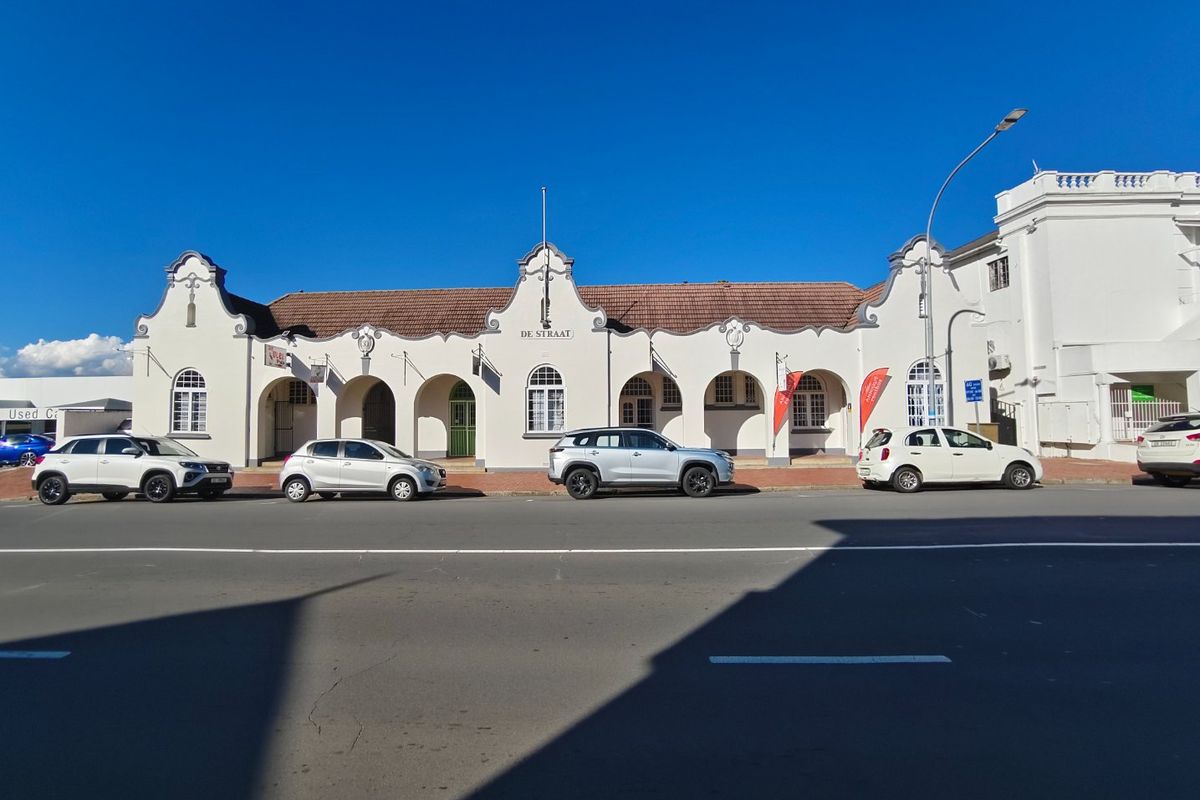 Street-facing view of a commercial building featuring a distinctive gabled facade, arched colonnade, and tiled roof architecture.