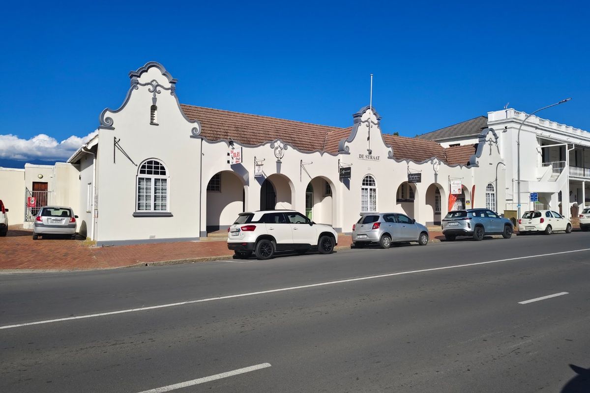A well-maintained commercial building featuring a distinctive gabled facade, arched colonnade, and tiled roof, situated along a street with convenient parking.