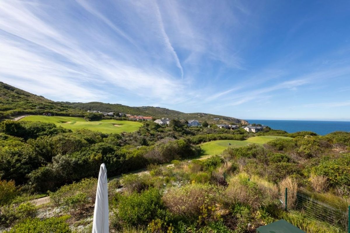 A scenic elevated view overlooking a coastal golf course, rolling hills, and the ocean in the distance.