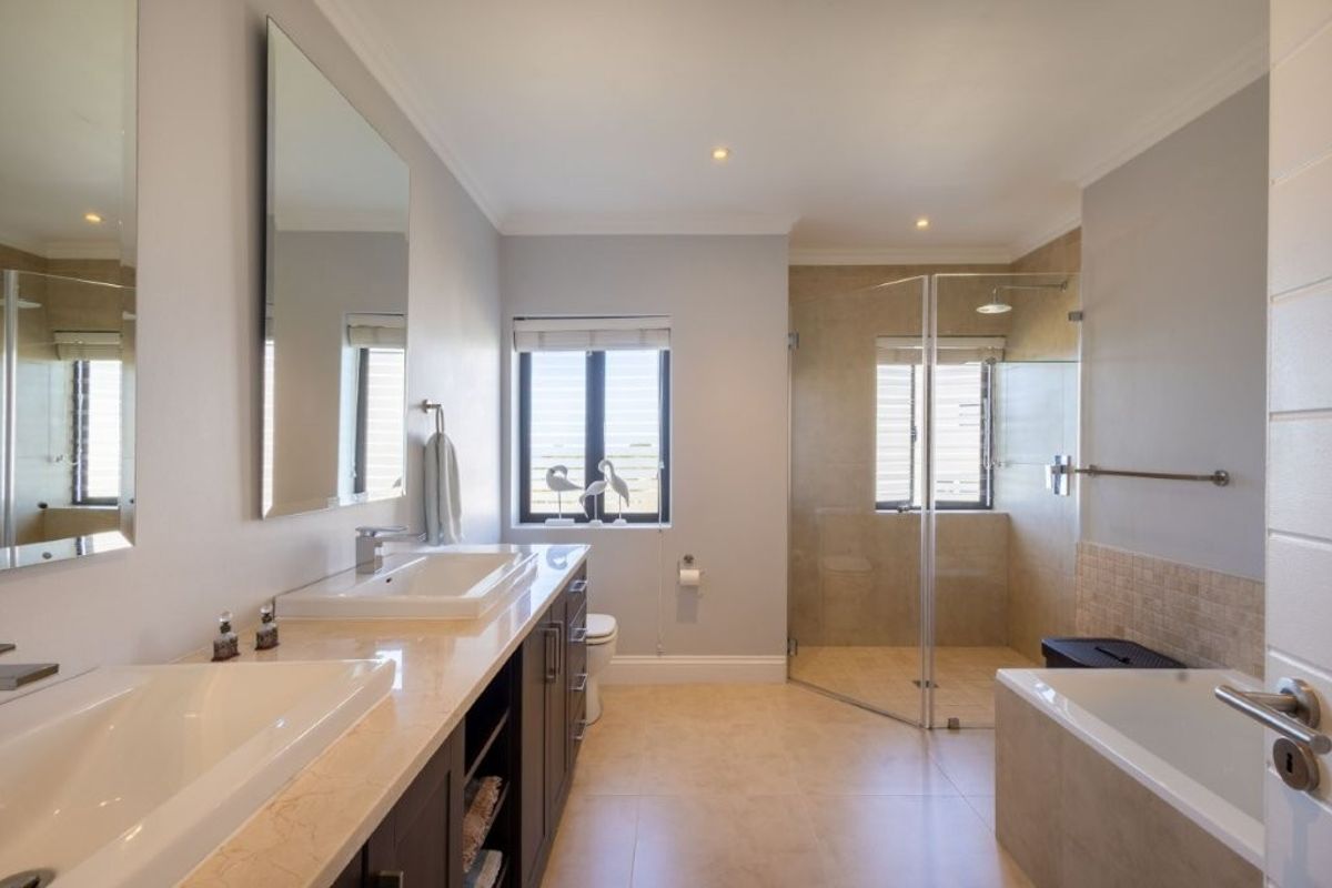 Modern bathroom featuring a double vanity with stone countertop, a glass-enclosed walk-in shower, and a separate bathtub with neutral tile finishes.