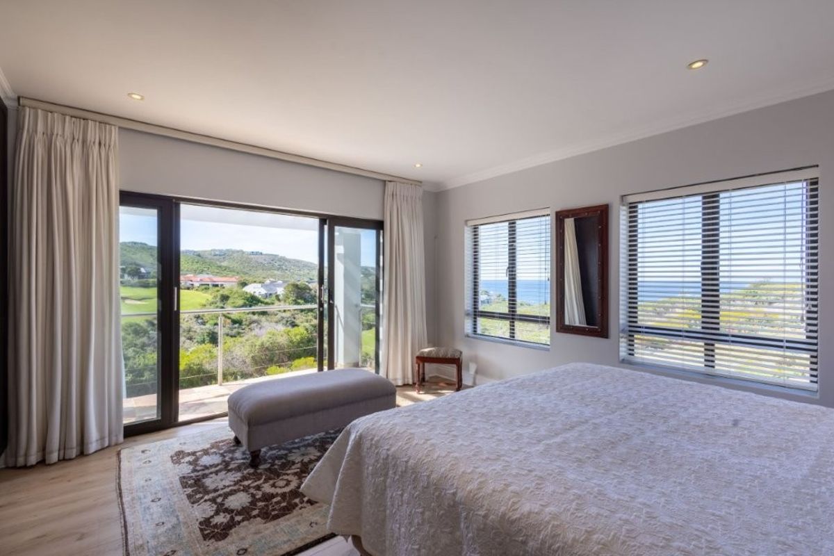 Spacious bedroom featuring large sliding glass doors opening to a private balcony with scenic coastal and landscape views, complemented by modern recessed lighting.