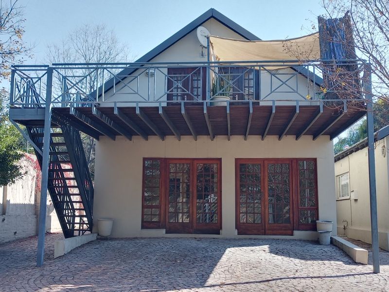 Rear elevation featuring a raised timber deck with metal staircase, accessible via double timber-framed glass doors, overlooking a paved courtyard area.
