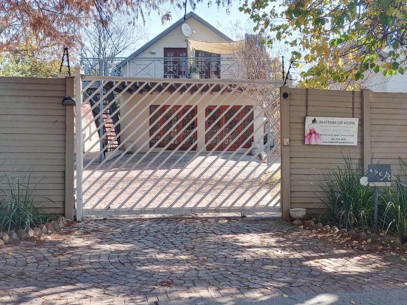 Front view of the property featuring a secure sliding gate, cobblestone driveway, timber fencing, and a double garage with an upper-level balcony.
