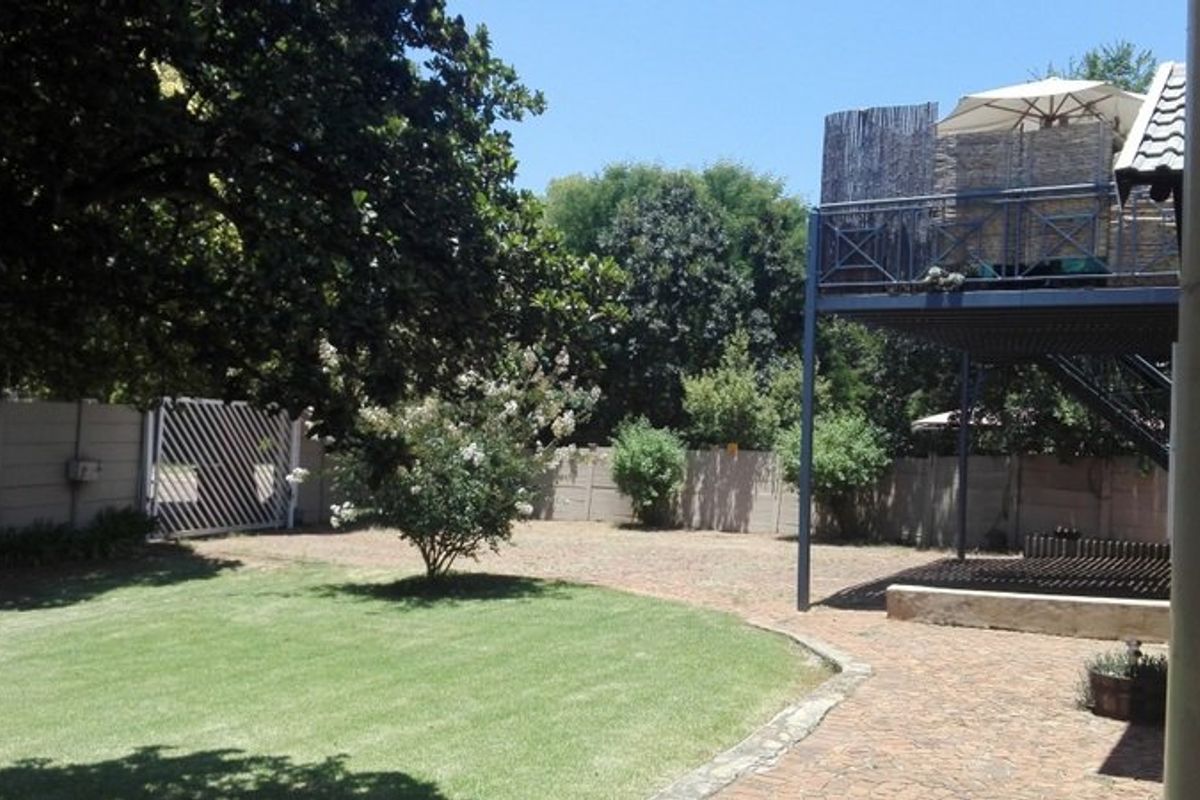 Spacious rear garden featuring a paved patio area, a well-maintained lawn, and an elevated balcony structure with metal stairs.