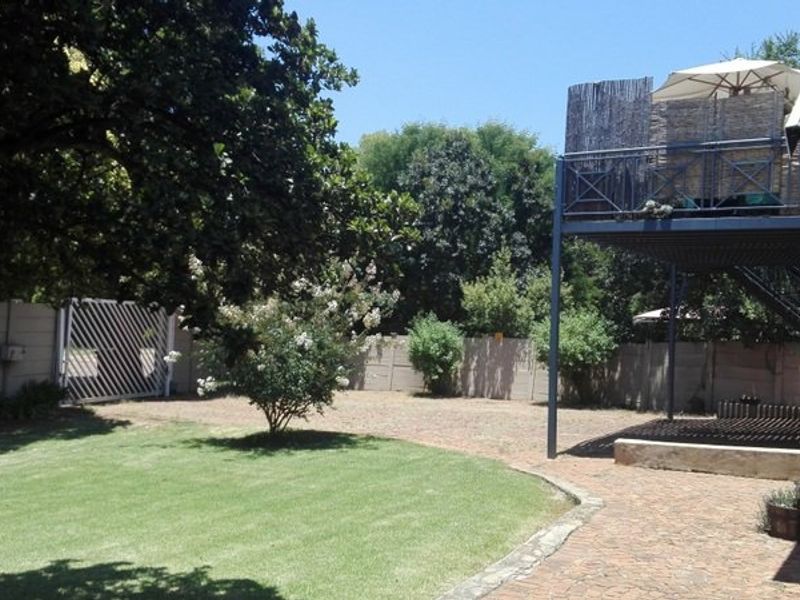 Spacious rear garden featuring a paved patio area, a well-maintained lawn, and an elevated balcony structure with metal stairs.