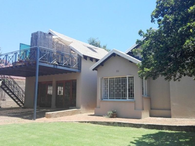 Rear view of the property featuring a raised deck with metal staircase, tiled roof, and a well-maintained garden area.