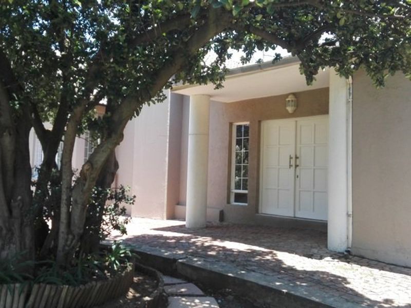 Front entrance featuring a covered porch with concrete columns, double doors, and a paved walkway leading to the main house entry.