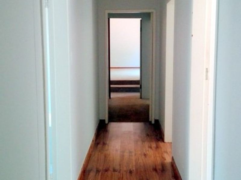 A clean, empty hallway featuring wood-look laminate flooring and neutral wall finishes, providing access to multiple rooms.