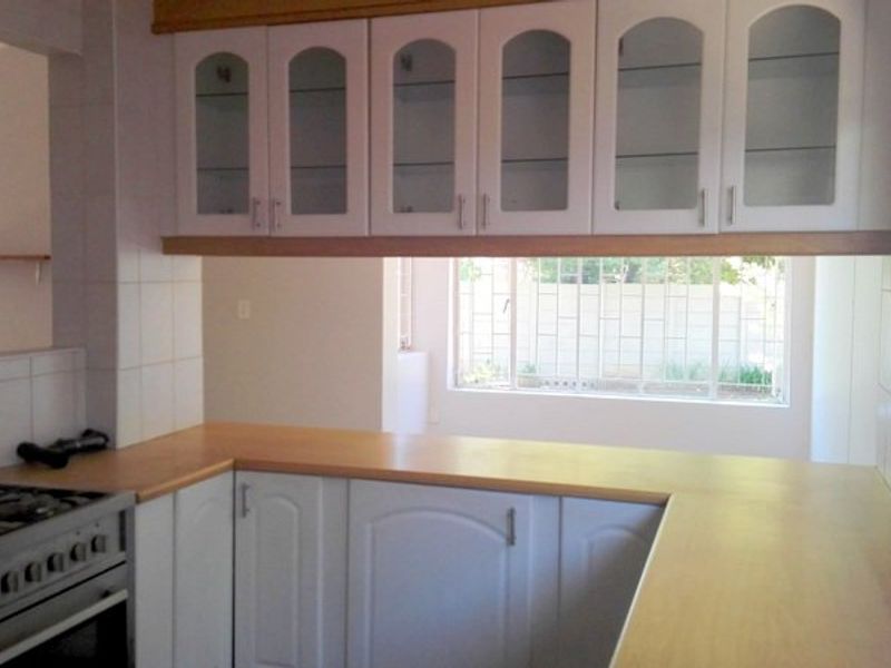 A functional kitchen featuring white cabinetry with glass-fronted uppers, laminate countertops, and a built-in gas stove, offering a clean and practical workspace.