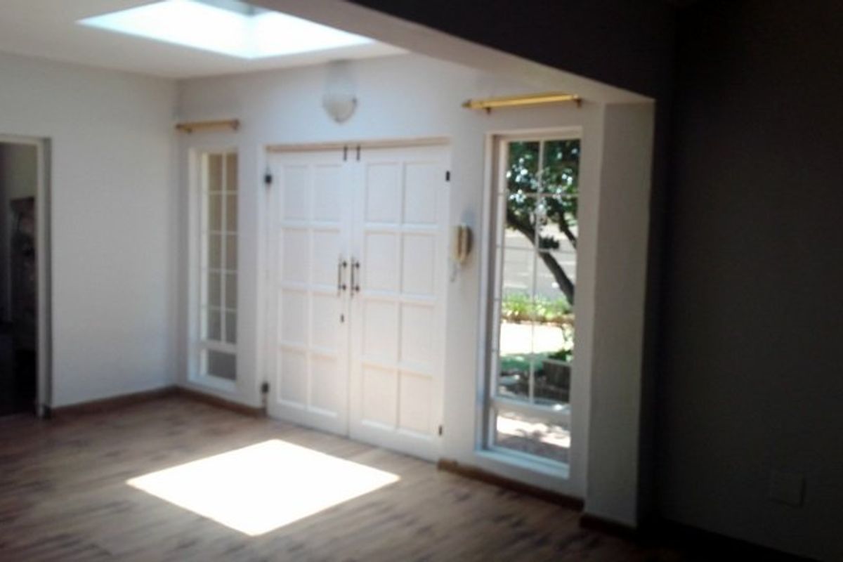 Bright living area featuring laminate flooring, a skylight, and double doors with sidelight windows providing natural light and garden access.
