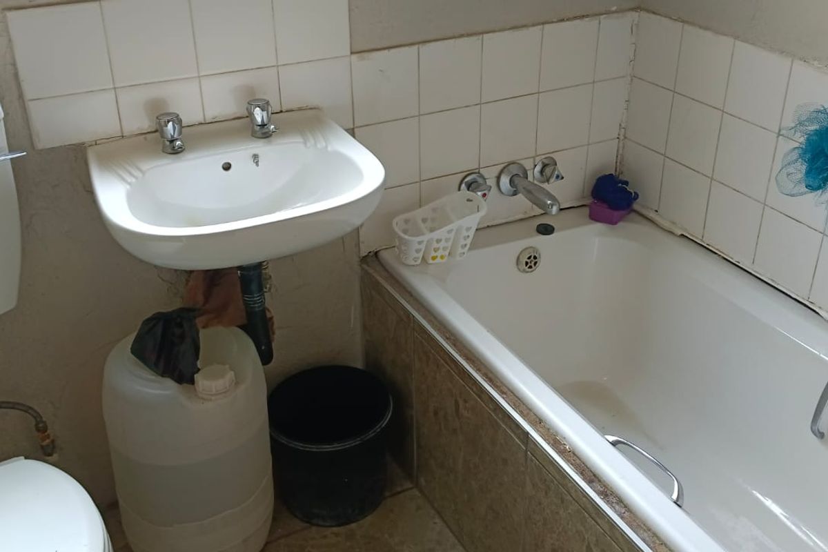 A dated bathroom featuring a standard bathtub, wall-mounted basin, and toilet, requiring cosmetic updates and maintenance to the wall finishes and tiling.