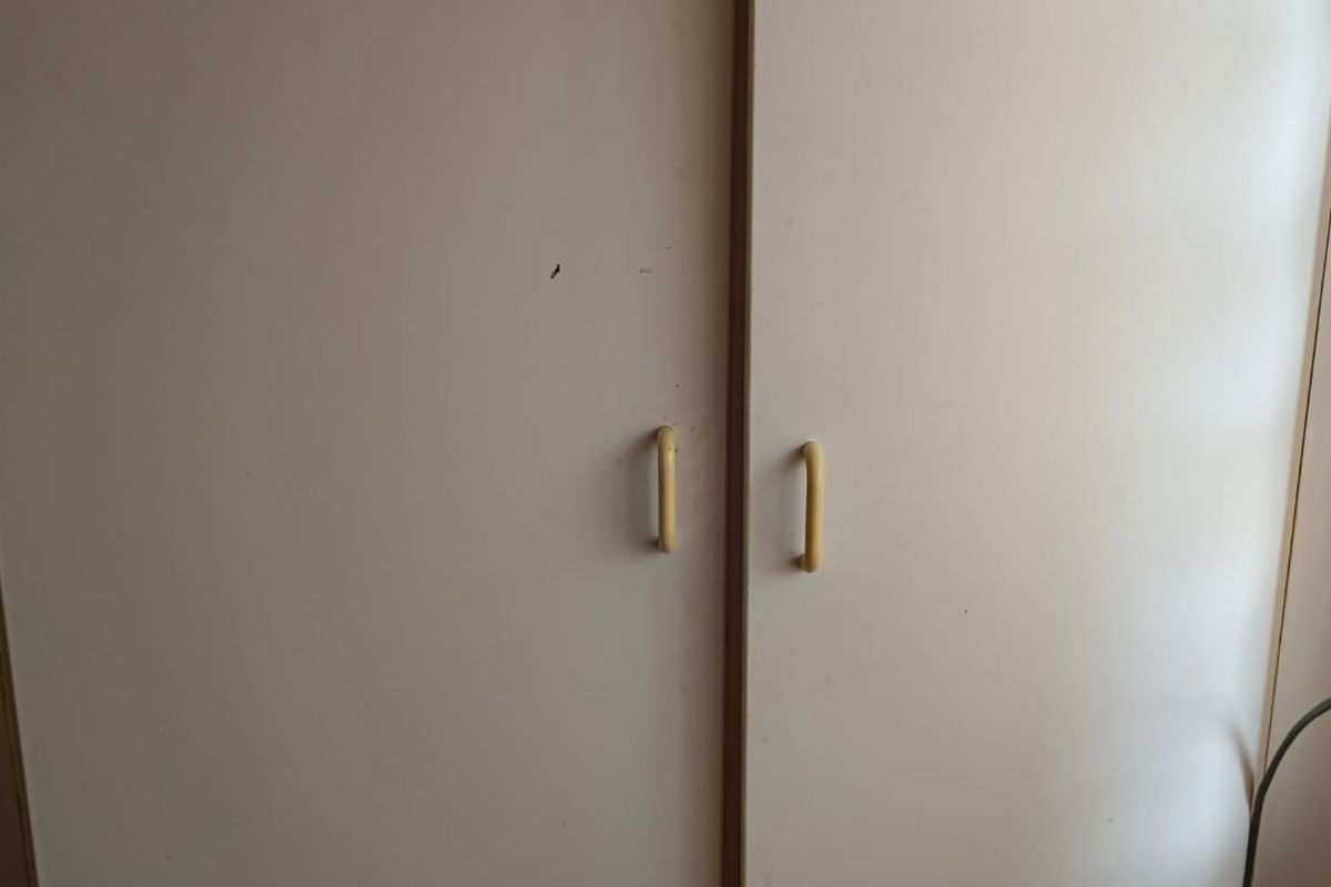 A close-up view of built-in bedroom cupboards featuring white laminate doors and dated plastic handles.