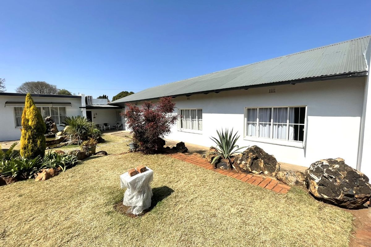 A rear view of the house featuring a well-maintained garden, brick pathways, and a corrugated metal roof.