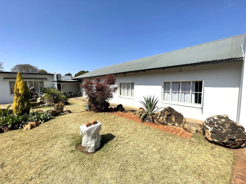 A rear view of the house featuring a well-maintained garden, brick pathways, and a corrugated metal roof.