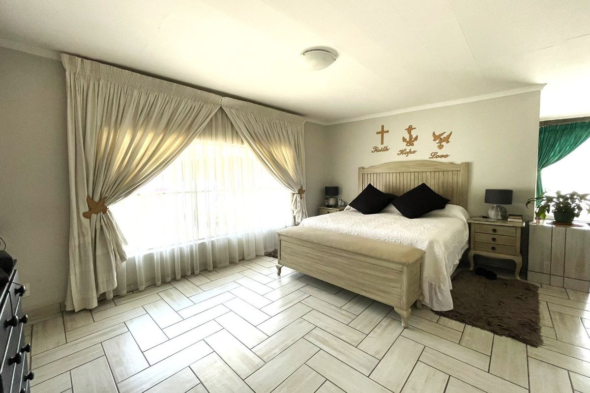 Spacious bedroom featuring modern herringbone tile flooring, neutral wall tones, and large windows with integrated curtain tracks.