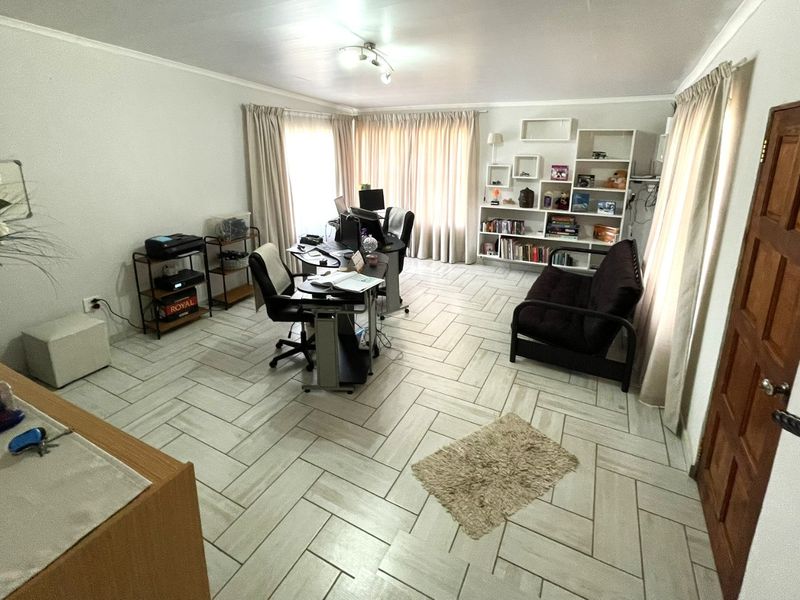 A functional home office space featuring light-toned herringbone tile flooring, built-in shelving, and neutral wall finishes, providing a versatile workspace.