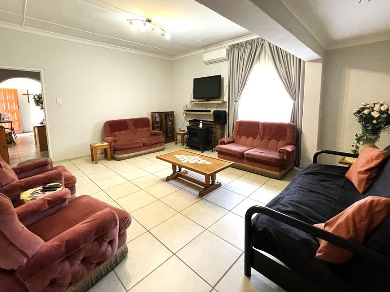 Spacious living room featuring neutral tiled flooring, cove cornicing, and a wall-mounted air conditioning unit, offering a comfortable and functional layout.
