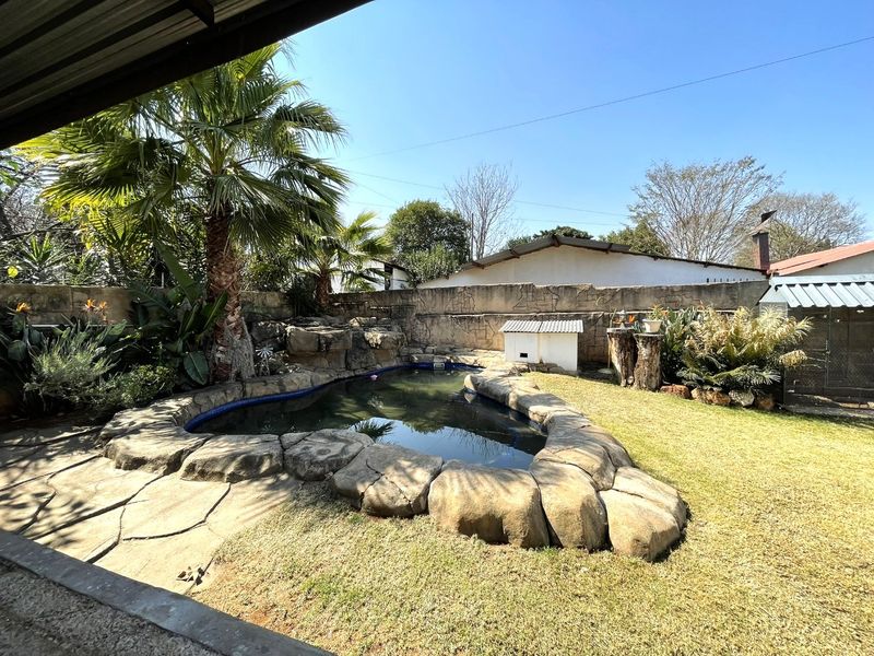 Outdoor pool area featuring a rock-style swimming pool, paved patio, and perimeter boundary wall in a landscaped garden setting.