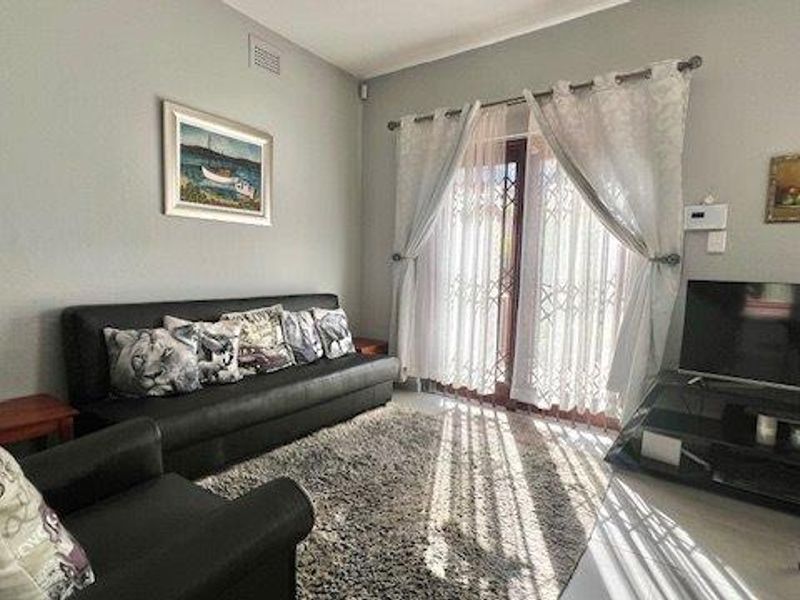 A comfortable living room featuring tiled flooring and sliding glass doors with security gates, providing direct access to the outdoor area.