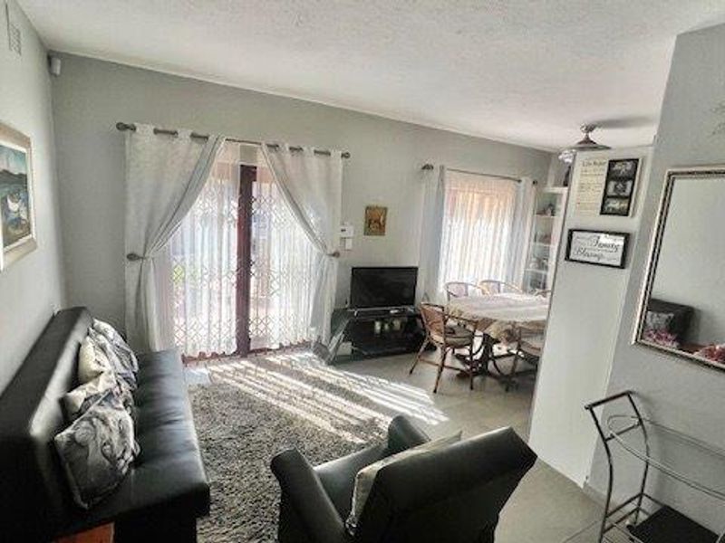 Open-plan living and dining area featuring tiled flooring, sliding glass doors with security gates, and neutral wall finishes.