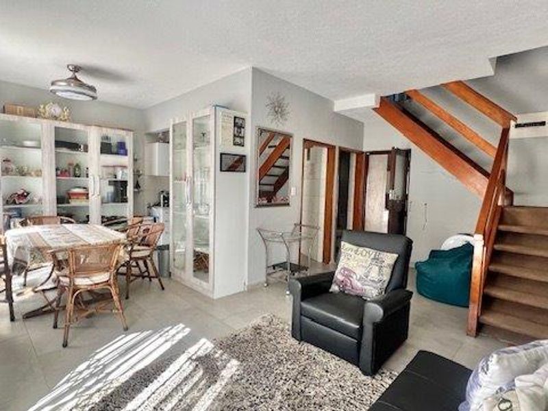Open plan living and dining area featuring tiled flooring, built-in display cabinetry, and a wooden staircase leading to the upper level.