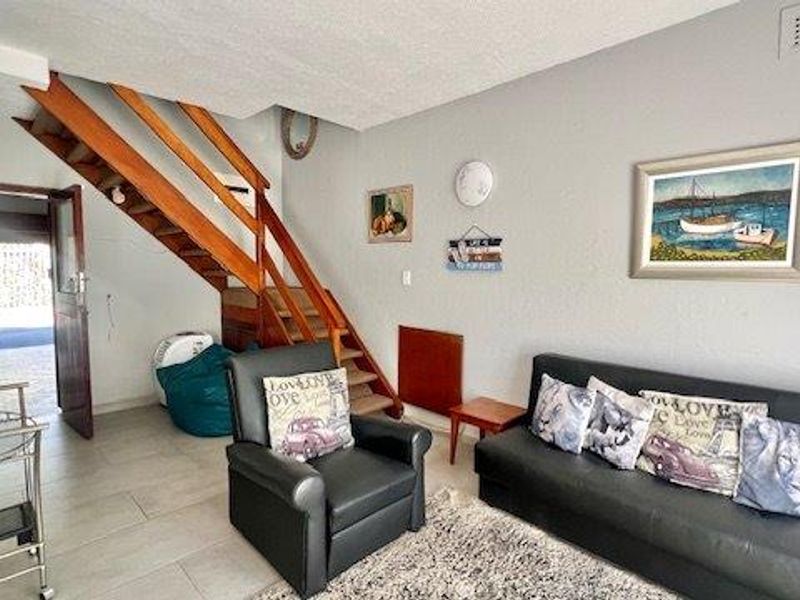 Open plan living area featuring tiled flooring and a wooden staircase leading to the upper level, with direct access to the exterior.