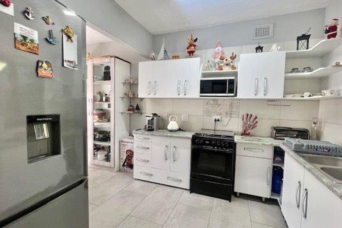 Functional kitchen featuring white cabinetry, tiled splashbacks, stone-look countertops, and a double basin sink, with an adjacent scullery area.