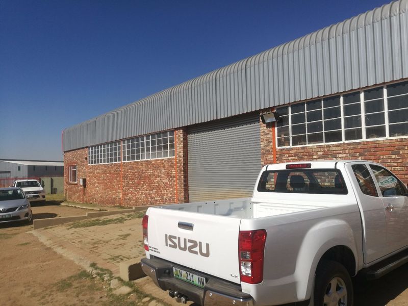 Industrial warehouse exterior featuring a face brick facade, corrugated metal roofing, and a large roller shutter door for vehicle access.