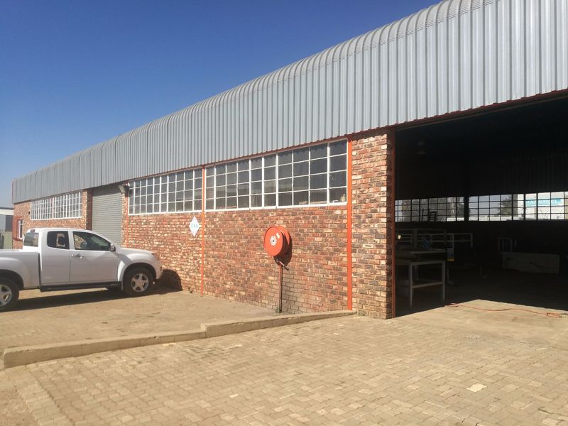 Industrial warehouse facility featuring a face brick facade, corrugated metal roofing, large roller shutter access, and a paved exterior driveway area.
