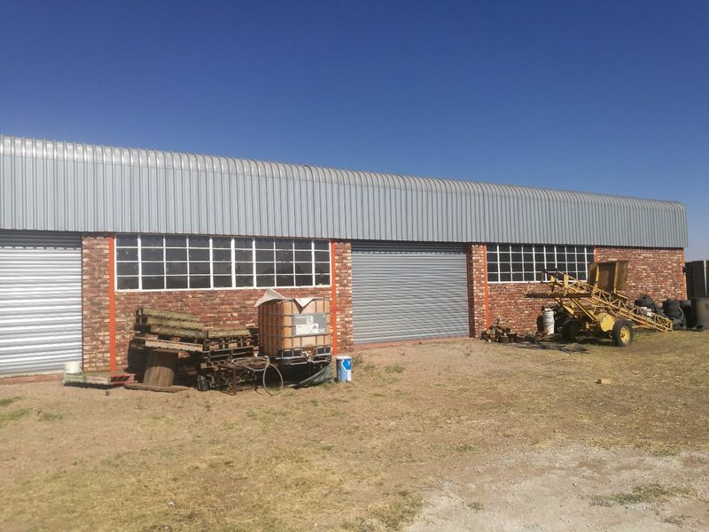 Rear view of an industrial warehouse building featuring face brick walls, corrugated metal roofing, and multiple roller shutter access doors.