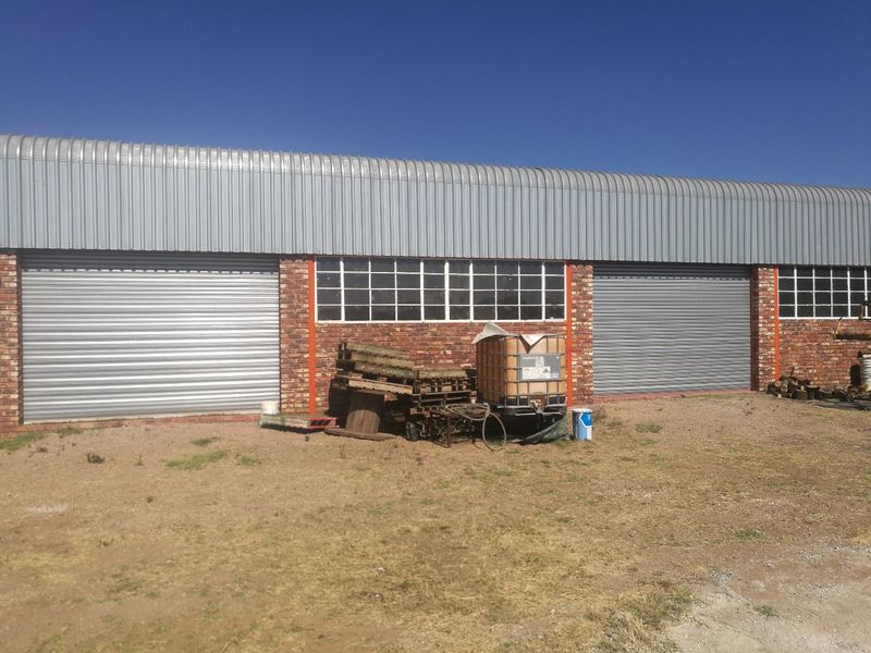 Industrial warehouse exterior featuring corrugated metal roofing, brick facade, and multiple roller shutter doors with steel-framed windows.