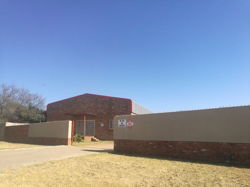 Front view of an industrial property featuring a brick facade, metal roofing, and a secure perimeter wall with security spikes.