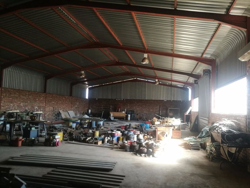 Spacious industrial warehouse featuring exposed steel portal framing, corrugated metal roofing, brick walls, and durable concrete flooring, suitable for various storage or workshop applications.